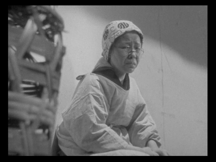 A frame from the last few seconds of Ozu's The Only Son, showing the mother seated outside the silk mill, anguish on her face.